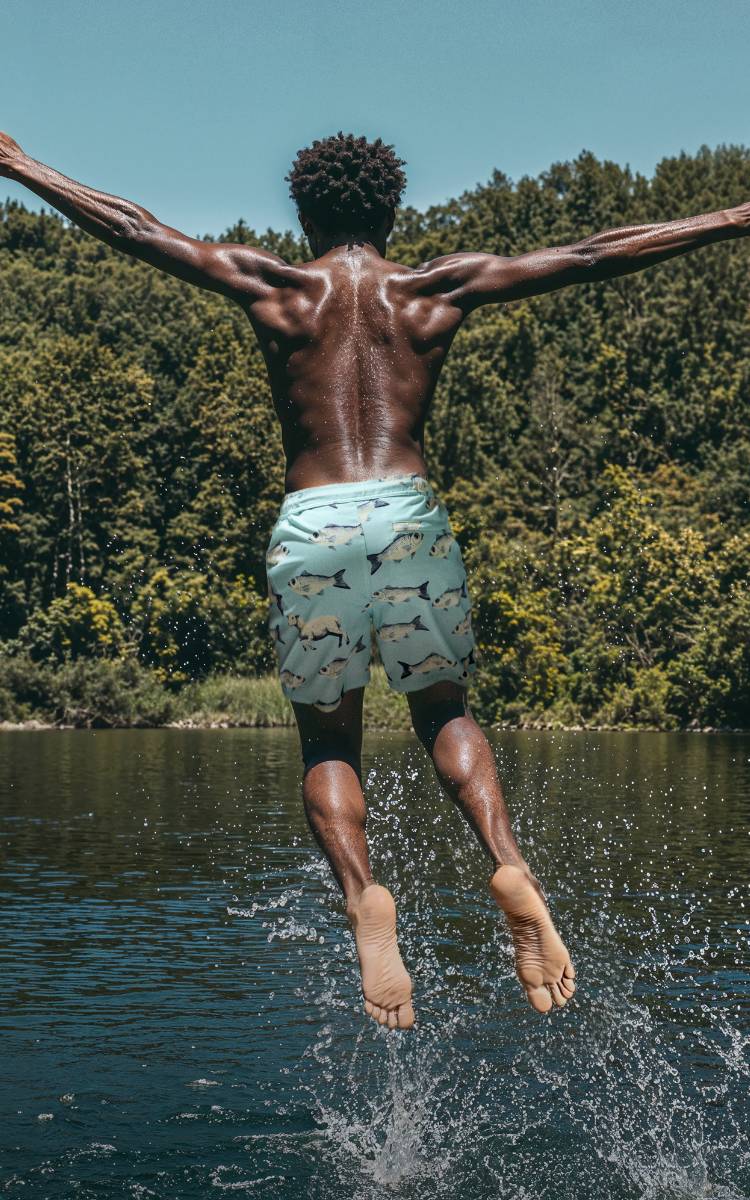 A male model wearing merino swim shorts jumping in to a lake. A female model wearing the Wave Polo Shirt.