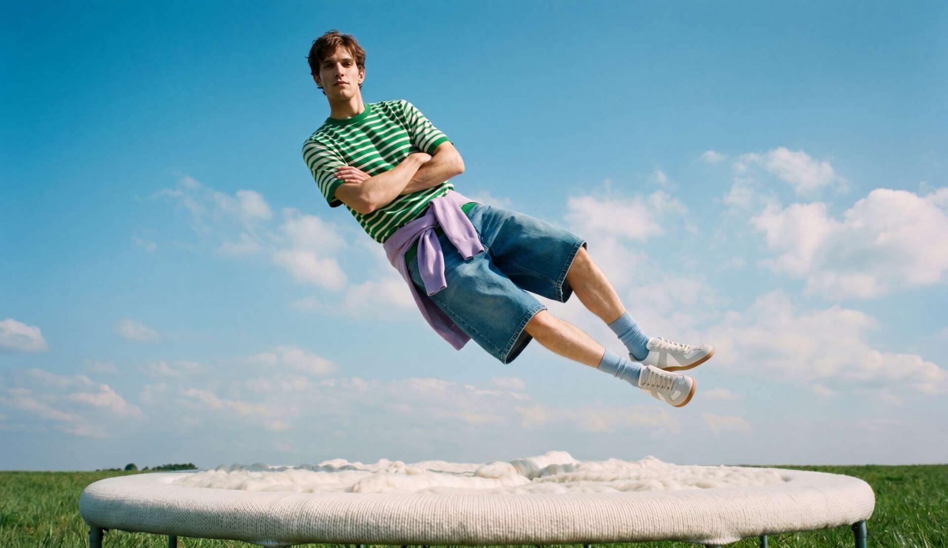 Model suspended mid-air above a wool-covered trampoline in an open field